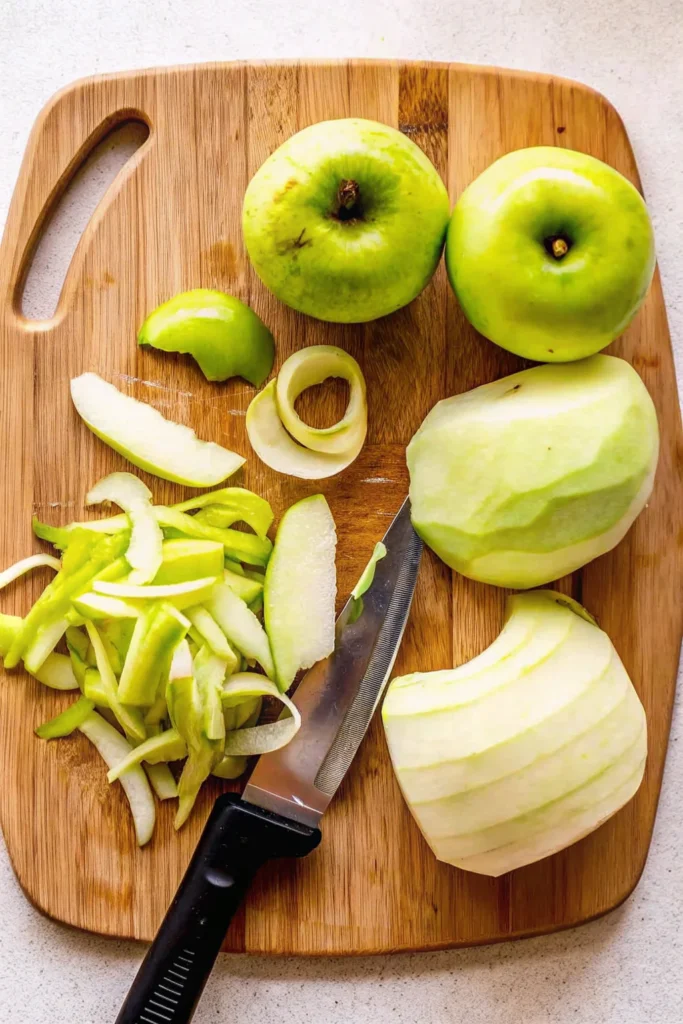 Freshly peeled and sliced Granny Smith apples on a wooden cutting board, ready for making apple puff pastry.